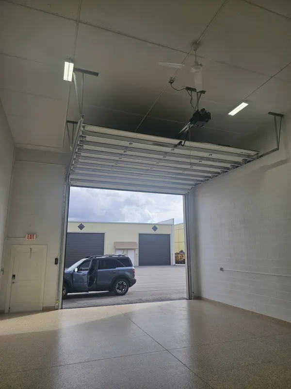 Tall overhead door open on a garage condo with paved drive outside