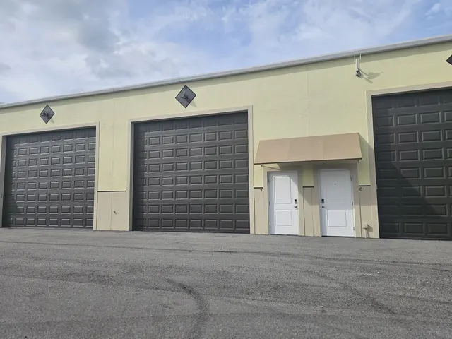 Row of garage condo units with dark overhead doors, entry doors and security camera